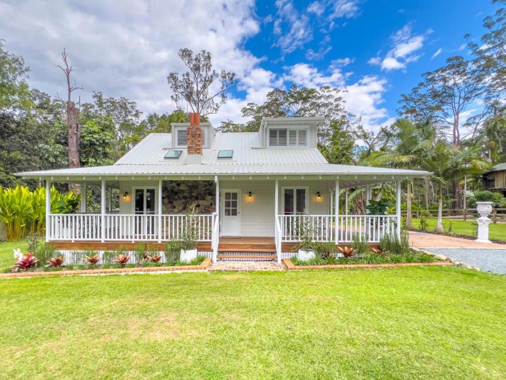 een wit huis met een veranda en een gazon bij The Gingerbread House in Upper Tallebudgera