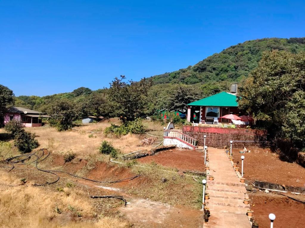 a house in a field with a mountain in the background at Junglee Valley Holiday Home in Mahabaleshwar