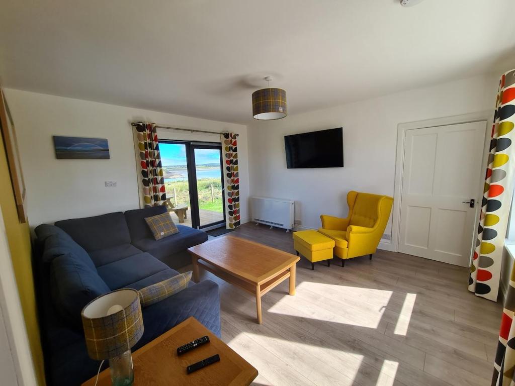 een woonkamer met een blauwe bank en gele stoelen bij Beachcroft Cottage in Aird Tong