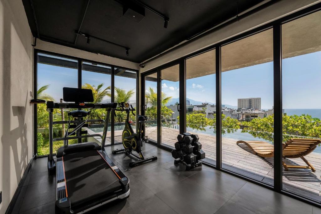 A compact glass-fronted gym with cardio equipment, weights and an ocean glimpse.
