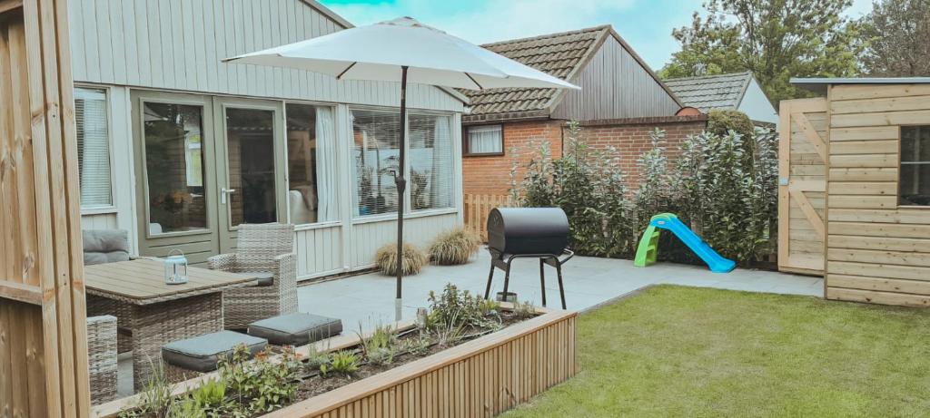 een terras met een parasol en een stoel en een speeltuin bij The Pelican in Schoorldam