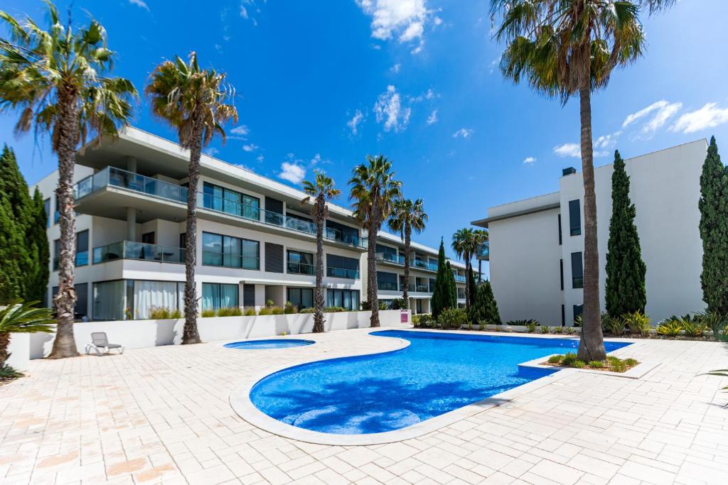 an exterior view of a building with palm trees and a swimming pool at Cavalo Preto Ocean Breeze Apartment in Forte Novo Quarteira in Quarteira