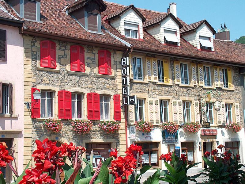 ein Gebäude mit roten Fenstern und Blumen davor in der Unterkunft Hôtel de la Croix-Blanche in Cressier