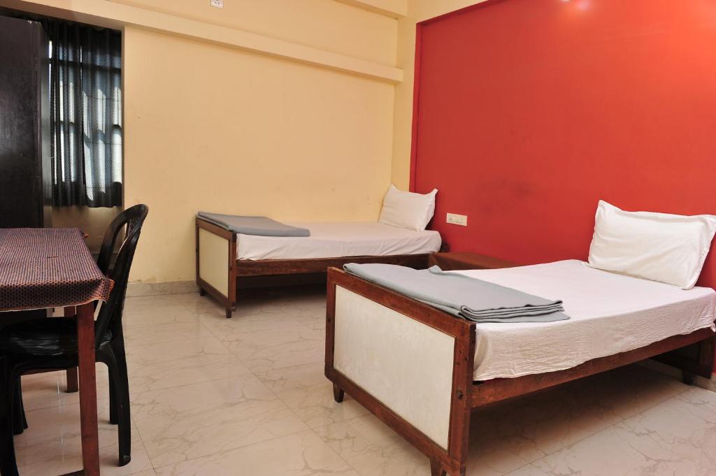 twee bedden in een kamer met een rode muur bij Alfa Tourist Home, Batheri in Sultan Bathery