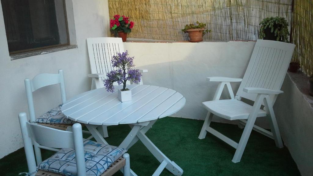2 weiße Stühle und ein Tisch mit einer Vase Blumen in der Unterkunft Dommu Asile in Baunei
