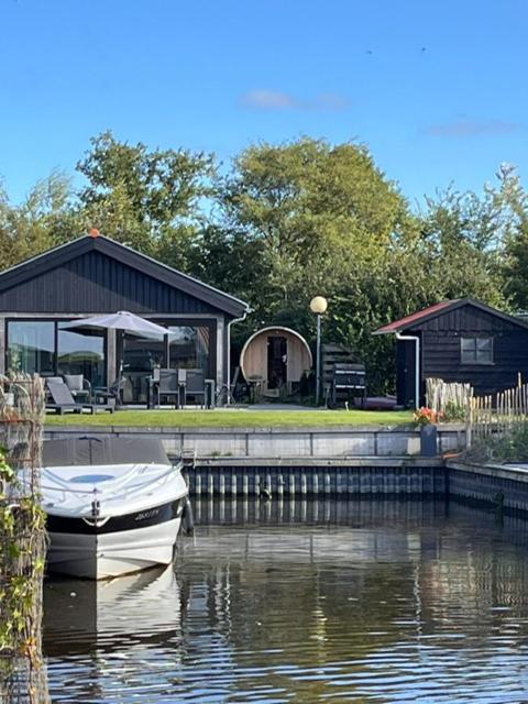 a boat sitting on the water next to a house at Lauwershuisje, Sauna, Harbour Lauwersmeer in Anjum