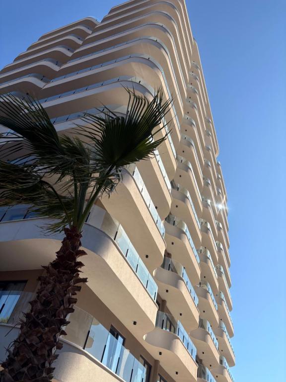a tall building with a palm tree in front of it at Rezidenca Onda in Lezhë