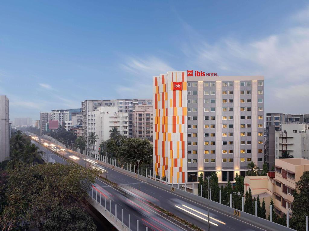 a large building with an orange and white facade next to a highway at ibis Mumbai BKC in Mumbai