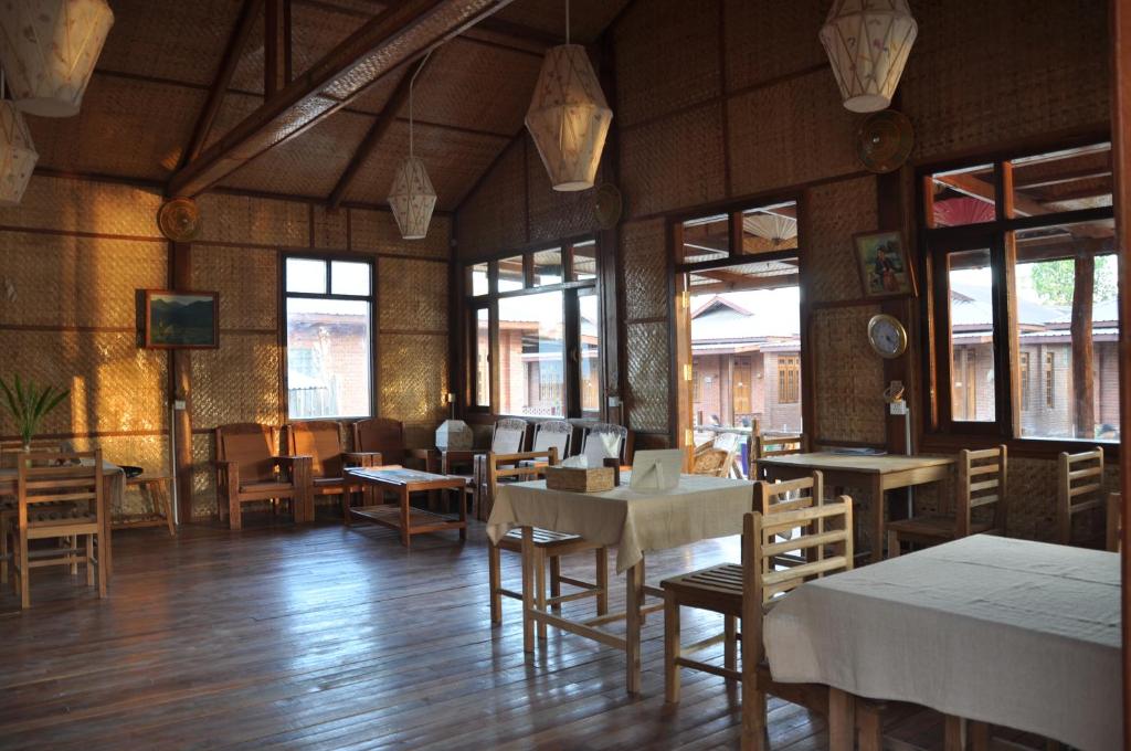 una sala da pranzo con tavoli, sedie e finestre di Trinity Family Inn a Nyaung Shwe