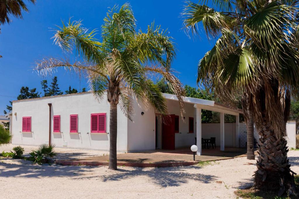 a white building with red shuttered windows and palm trees at Villa Mello in Torre Lapillo