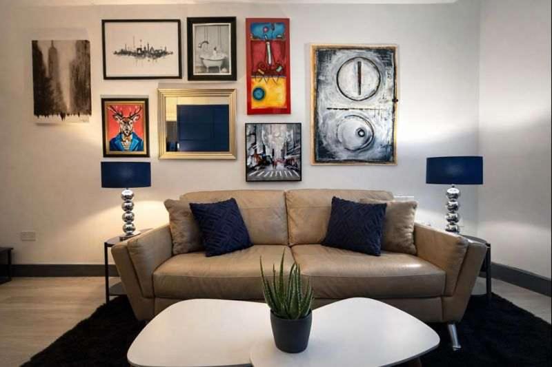 un soggiorno con divano e immagini appese al muro di The Plaza, King 1 Bedroom Suite by The Hive WA1 a Warrington