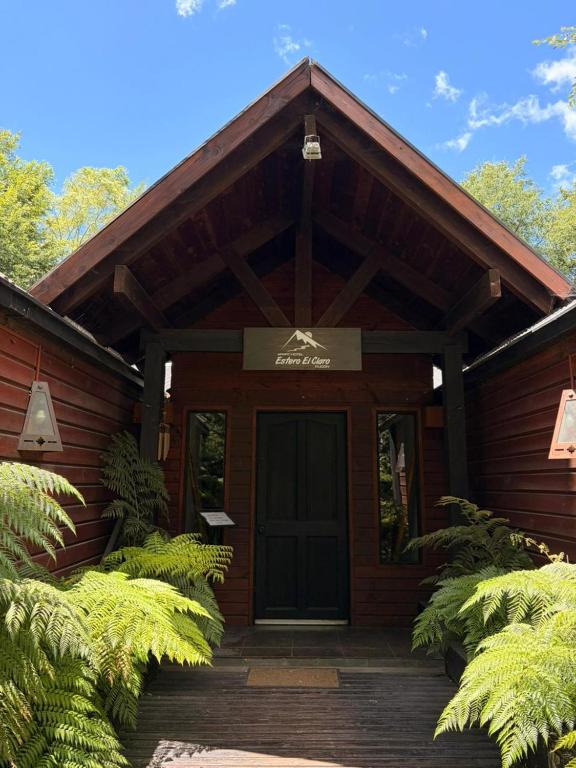 a wooden cabin with a black door and some plants at Estero El Claro Hotel y Cabañas in Pucón