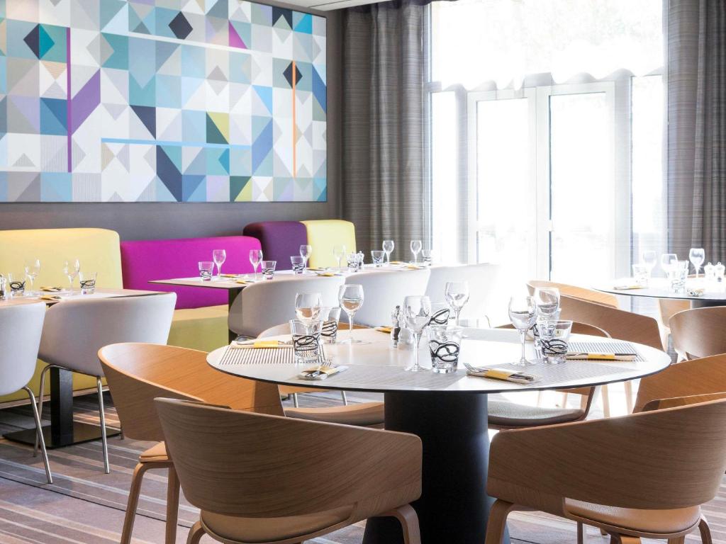 a restaurant with white tables and chairs and a colorful wall at Novotel Saint-Quentin en Yvelines in Magny-les-Hameaux