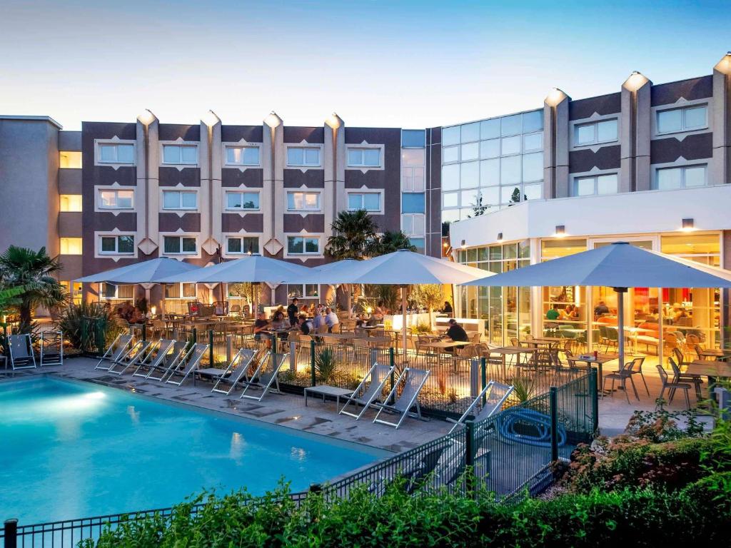 a hotel with a pool and chairs and umbrellas at Novotel Clermont-Ferrand in Clermont-Ferrand
