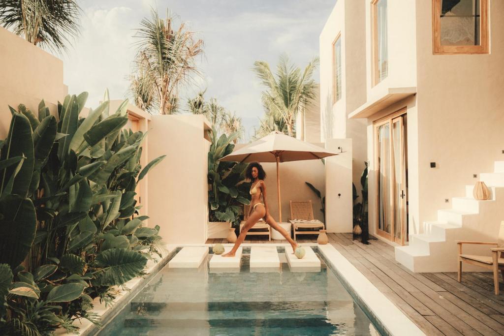 a woman in a bikini sitting next to a swimming pool at NORI Boutique Villas Uluwatu - Breakfast Available in Uluwatu