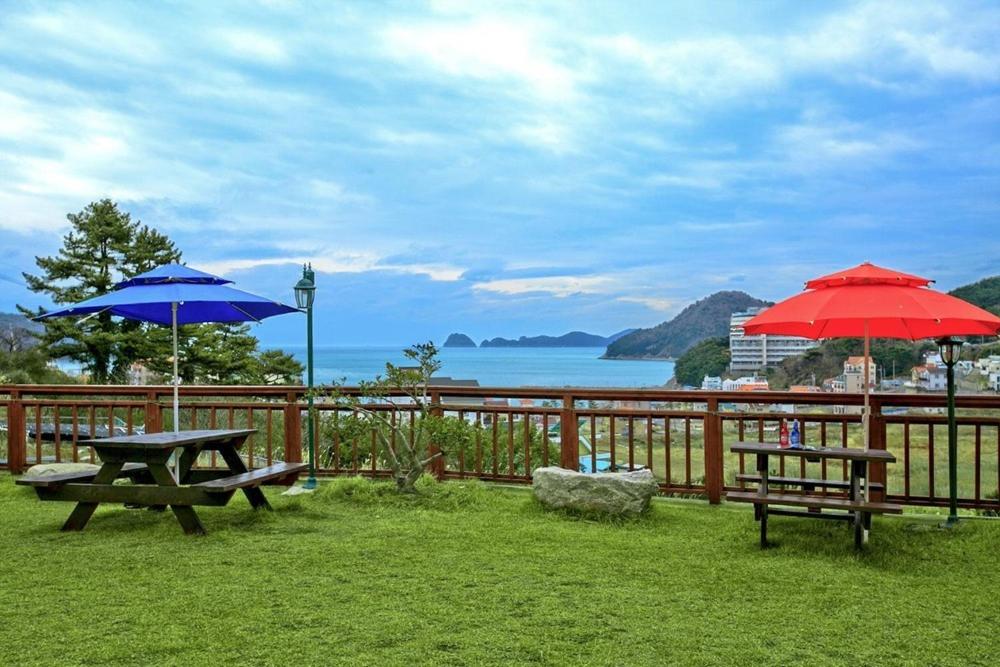 two picnic tables and two umbrellas in the grass at Geoje Haneul Ari Pension in Geoje