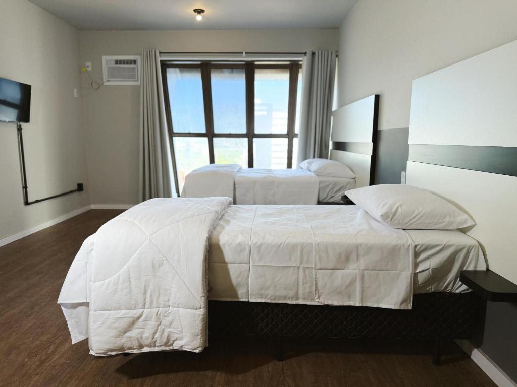 a bedroom with two beds with white sheets and a window at Smart Stay Lofts in Joinville