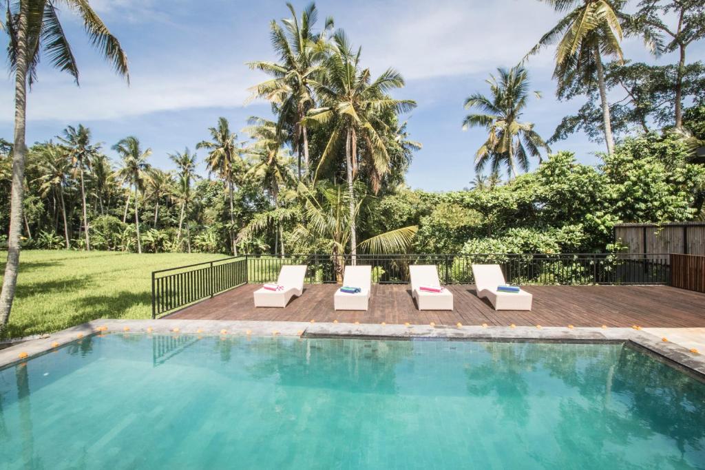 a swimming pool with two lounge chairs and palm trees at Serenity Villa & Spa in Ubud