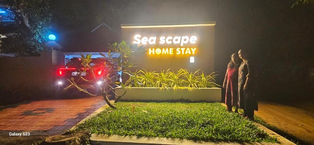 two people standing in front of a home stay sign at night at sea scape homestay in Mararikulam