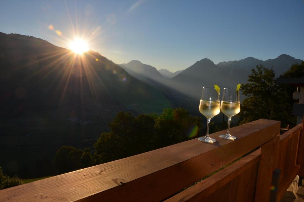 two glasses of wine sitting on a wooden railing with the sun in the background at Ferienwohnung La-Wurm in Hart im Zillertal
