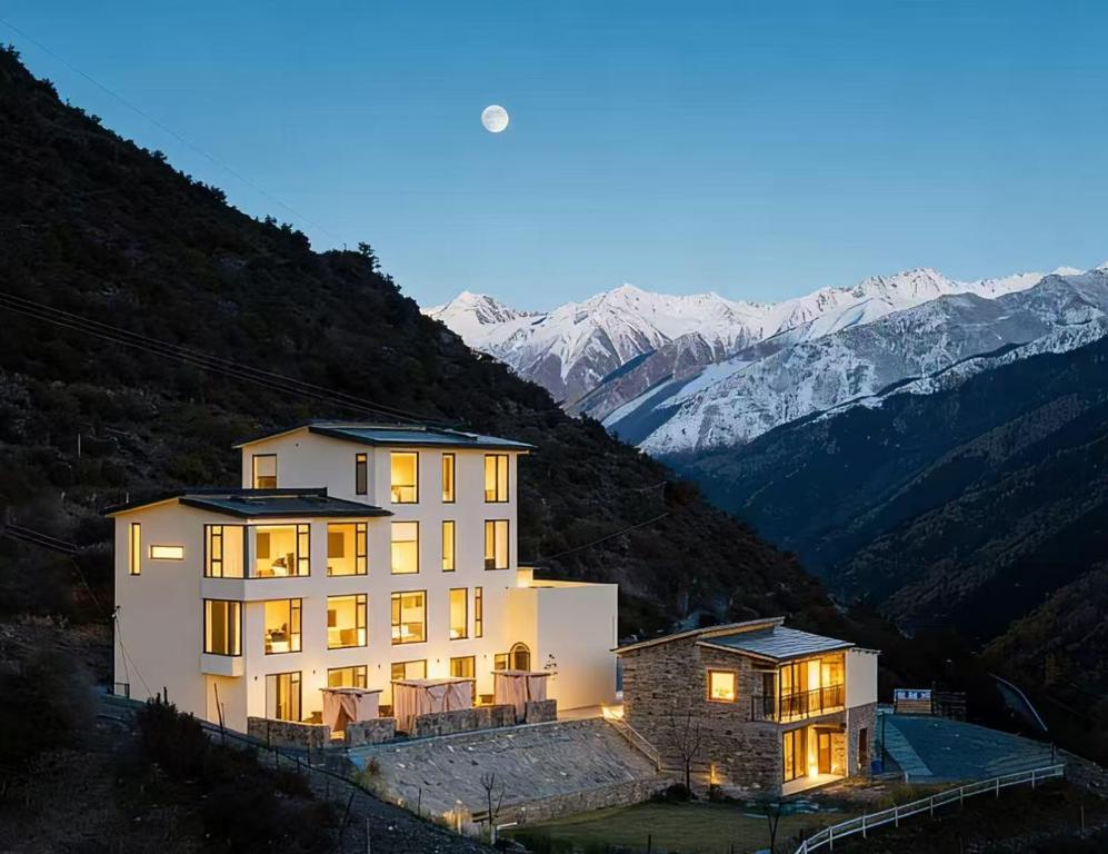a building on a hill with mountains in the background at Endless Summer Cloudscape Hot Springs Siguniang Mountain in Mount Siguniang