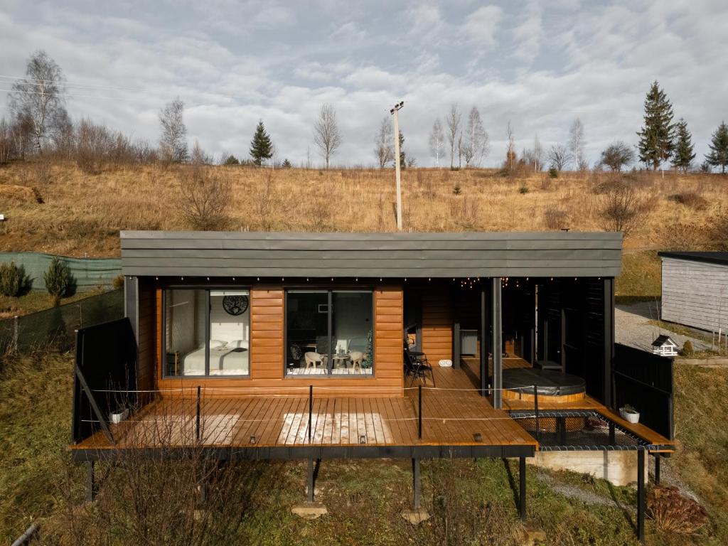 ein kleines Haus mit einer Holzterrasse auf einem Feld in der Unterkunft Ecottage котедж для двох у горах із чаном-джакузі in Slawske