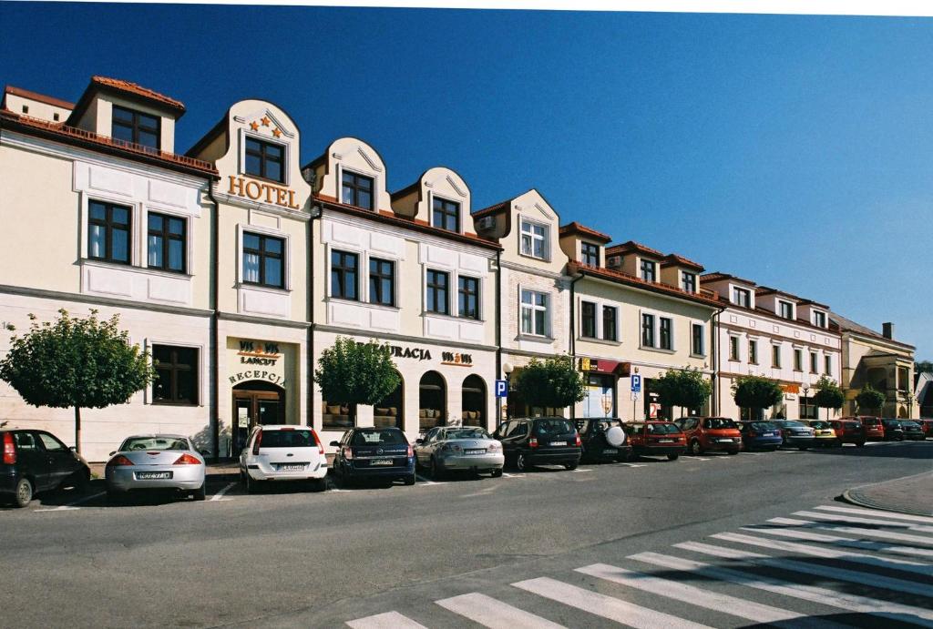 Hotel Vis a Vis Łańcut في وانسوت: مبنى ابيض كبير به سيارات تقف في موقف للسيارات
