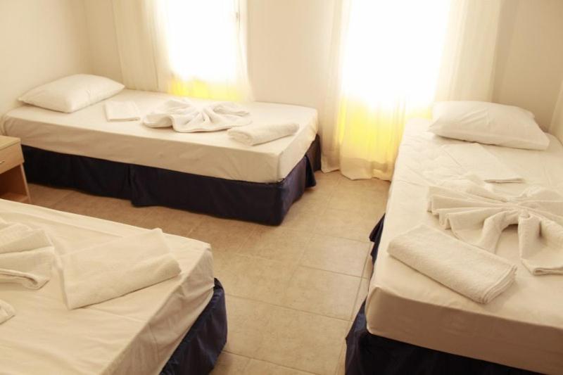 a room with three beds with white sheets and a window at Denizci Pension in Kaş