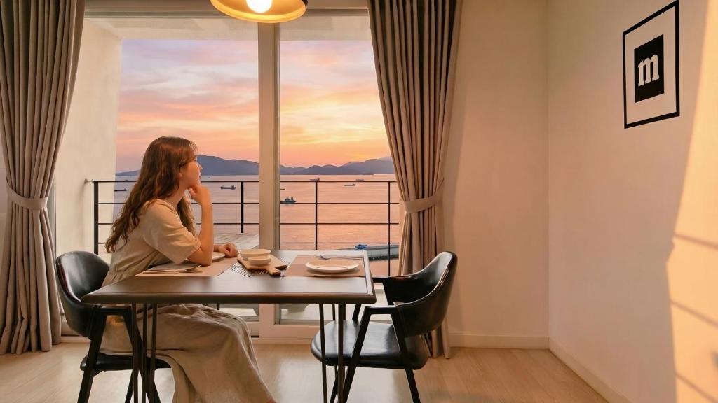una donna seduta a un tavolo davanti a una finestra di Yeosu Harushimpyo Pension a Yeosu