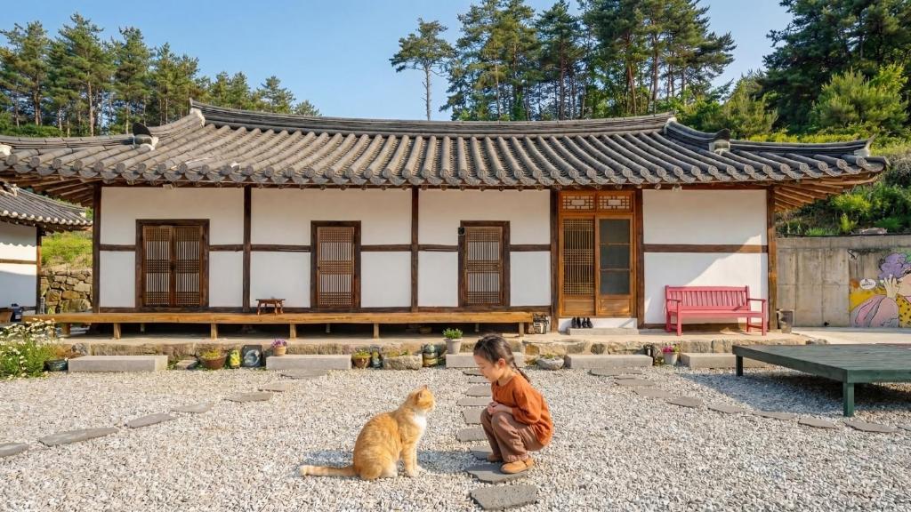 Un niño y un gato sentados frente a un edificio. en Gangneung ggabinejip hanok pension, en Gangneung