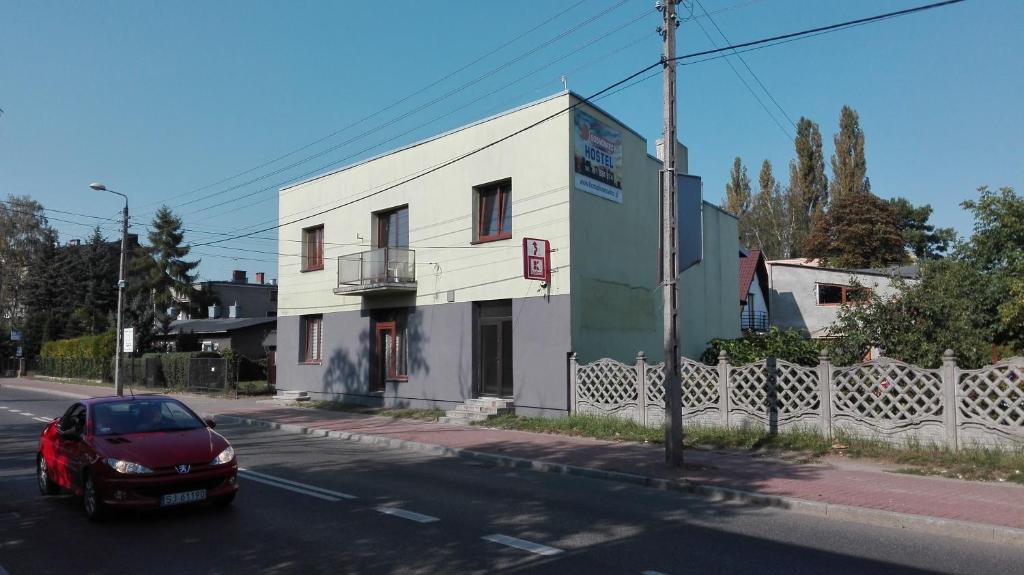 une voiture rouge garée devant un bâtiment blanc dans l'établissement Hostel Sosnowiec, à Sosnowiec