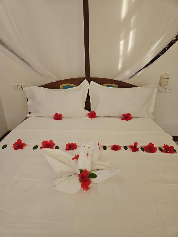 a bed with white sheets and red flowers on it at Upole HOTEL in Nungwi