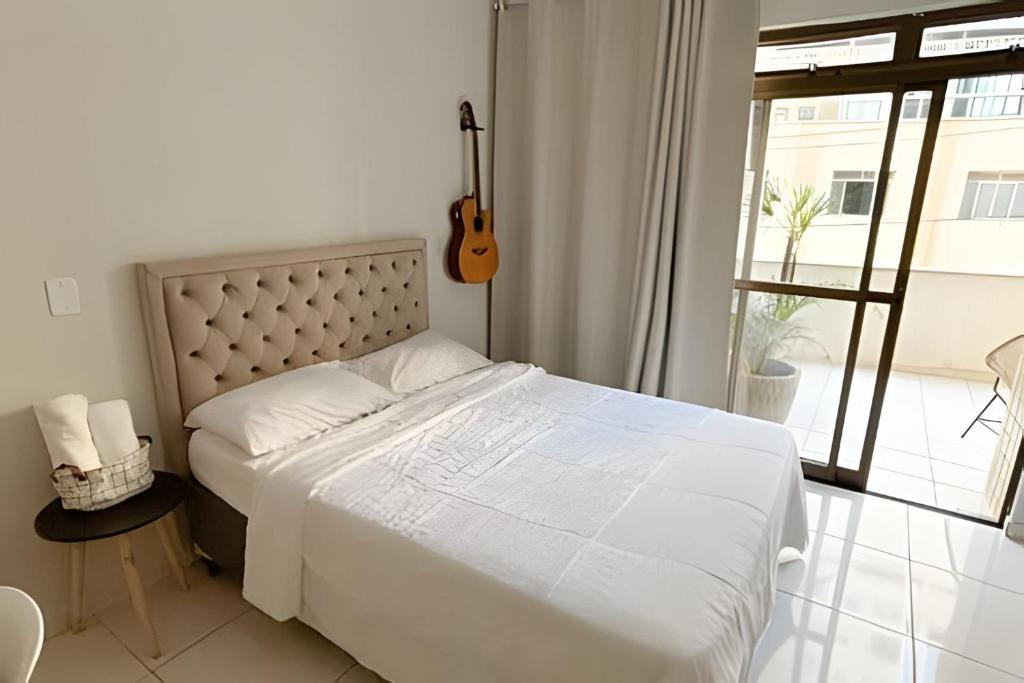 een wit bed in een slaapkamer met een gitaar bij No centro com Varanda, Smart Tv, Elevador e Garagem Paga in Viçosa