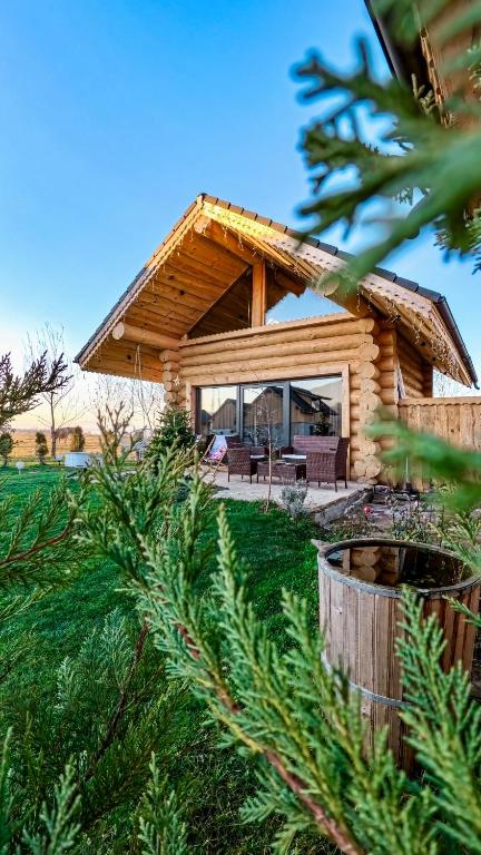a log house in a field with trees in the foreground at Cabana de la Stână in Râşnov