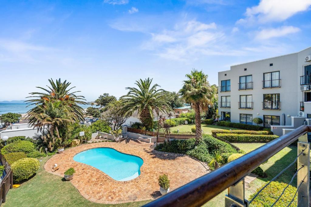 an apartment with a pool and palm trees and a building at Gordons Village View in Gordonʼs Bay