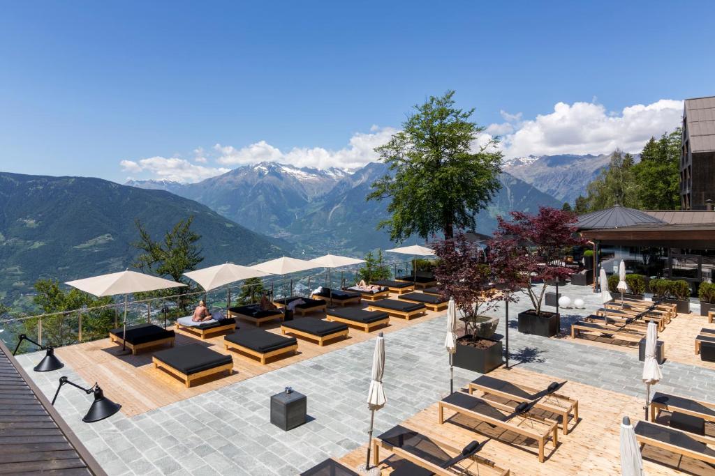 a hotel patio with lounge chairs and mountains in the background at Miramonti Boutique Hotel in Avelengo