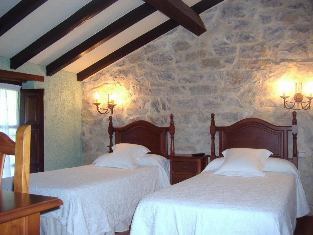 2 camas en una habitación con una pared de piedra en Posada Las Puentes, en Barcenilla