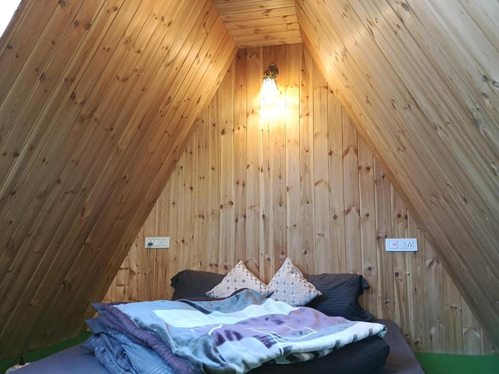 a bed in a room with a wooden wall at The Clifton chapter tirthan in Gushaini