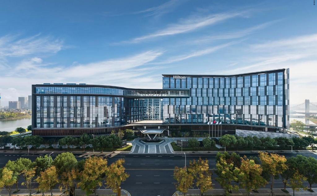 een groot glazen gebouw met een fontein ervoor bij Hilton Shaoxing Hotel And Residences in Shaoxing