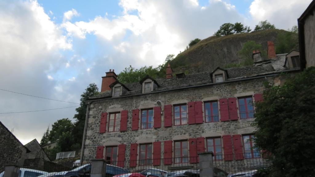 an old building with red windows and a hill at Relais des castors in Murat