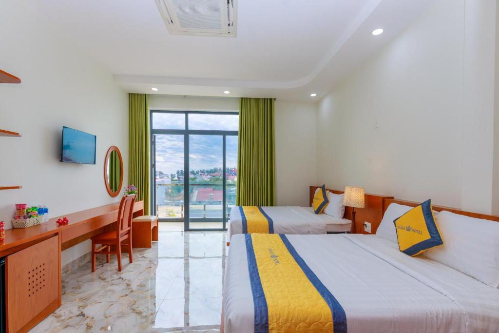 a hotel room with two beds and a desk and a window at Hanah Hotel Phan Thiet in Phan Thiet
