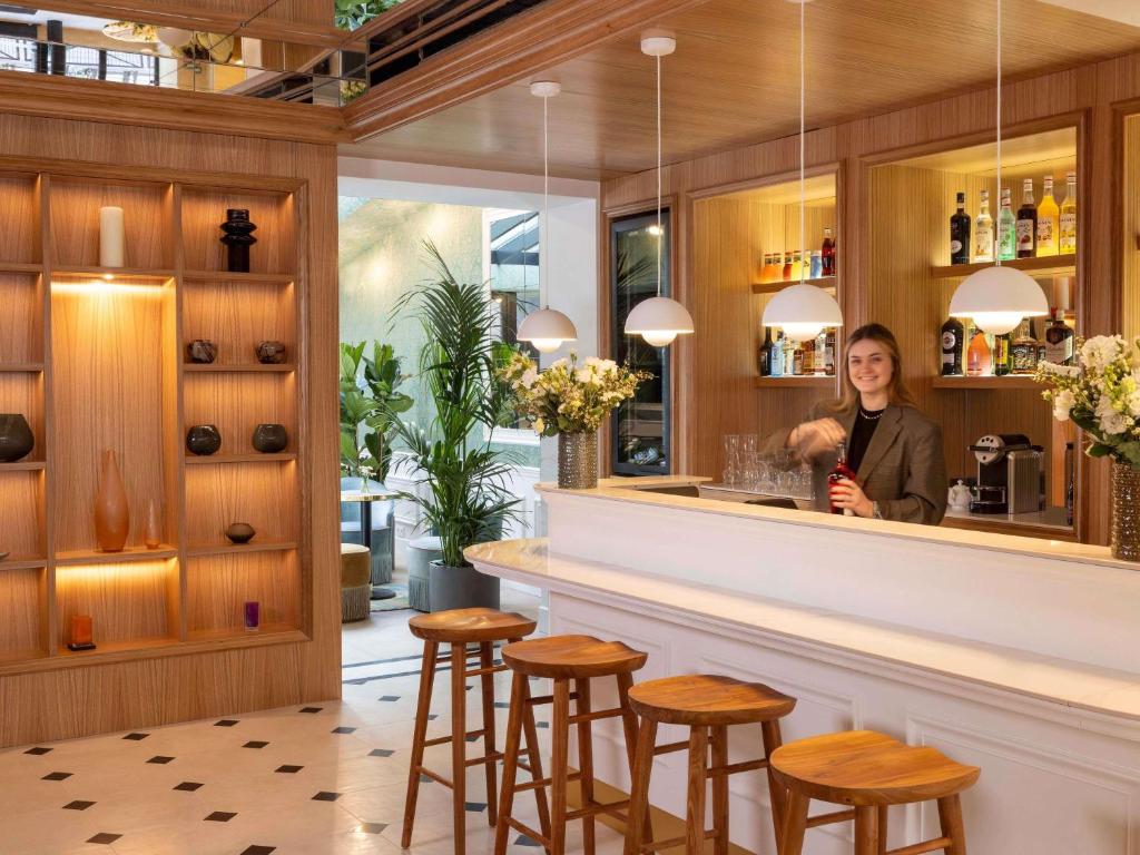 une femme debout derrière un bar dans un restaurant dans l'établissement Hotel Mercure La Sorbonne Saint-Germain-des-Prés, à Paris