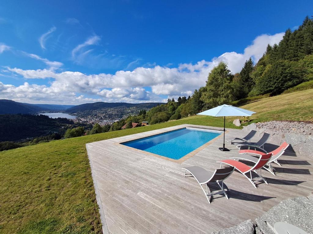 a swimming pool with chairs and an umbrella at Gîte Les Neufs Lieux in Gérardmer