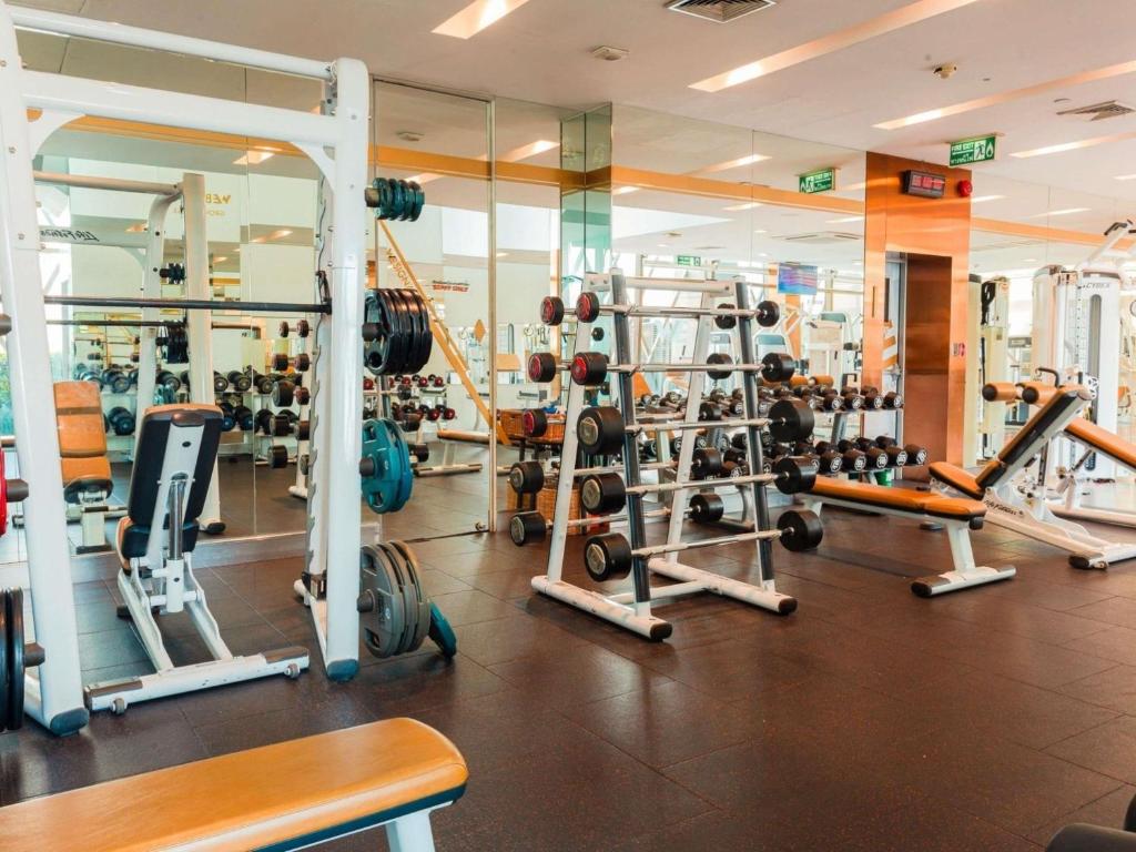 A mirrored strength-training gym contains racks, free weights, benches, and resistance machines.