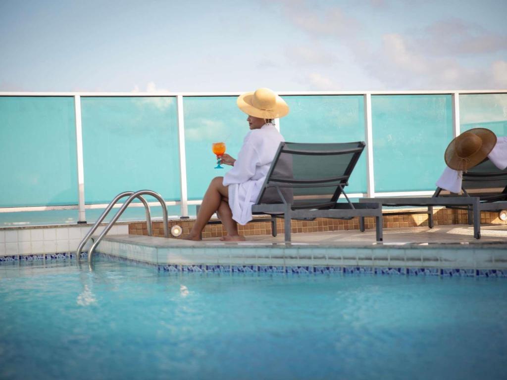 a woman sitting in a chair next to a swimming pool at Mercure Maceio Pajuçara in Maceió