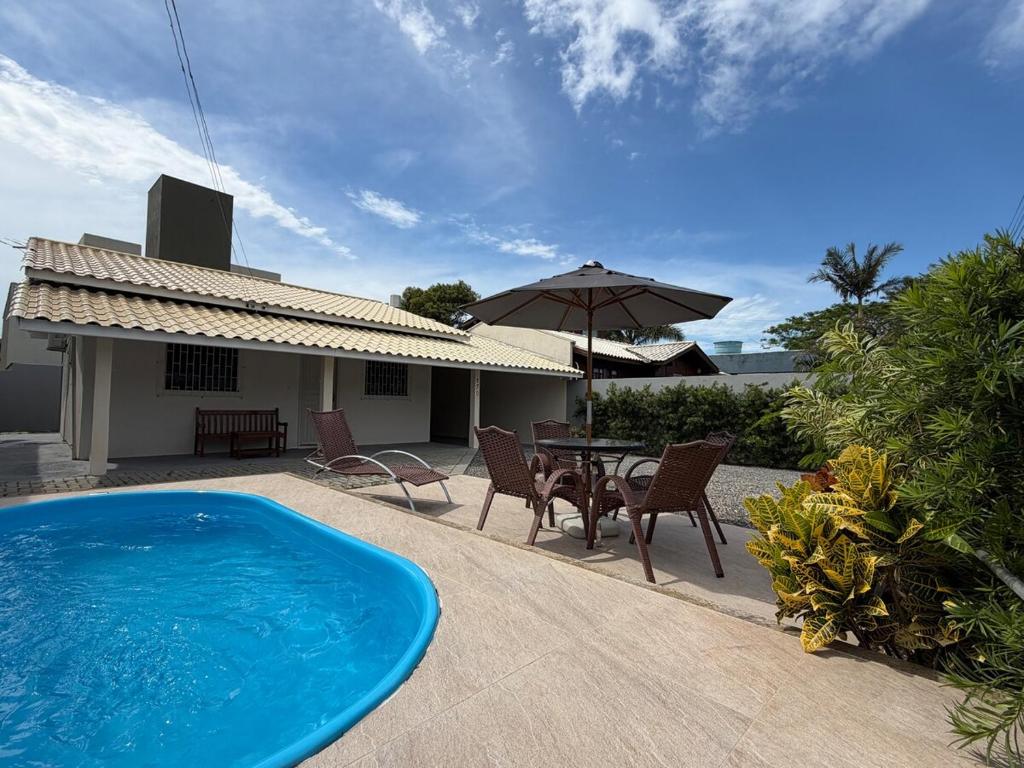 einen Pool mit Stühlen, einem Tisch und einem Sonnenschirm in der Unterkunft Casa Bombinhas Bombas beach in Bombinhas