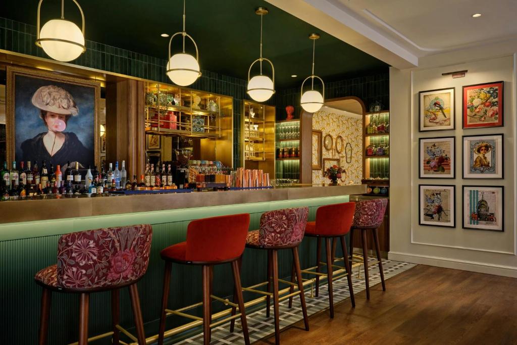 a bar with red chairs and a painting on the wall at The Cura Hotel Kensington, London, a Tribute Portfolio Hotel in London