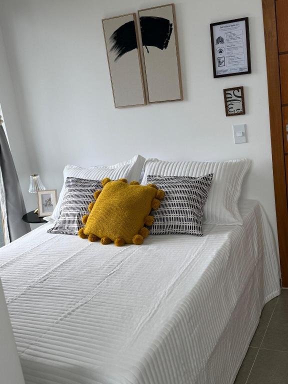 ein weißes Bett mit gelbem Kissen darauf in der Unterkunft Studio 218, Lavras, Minas Gerais in Lavras