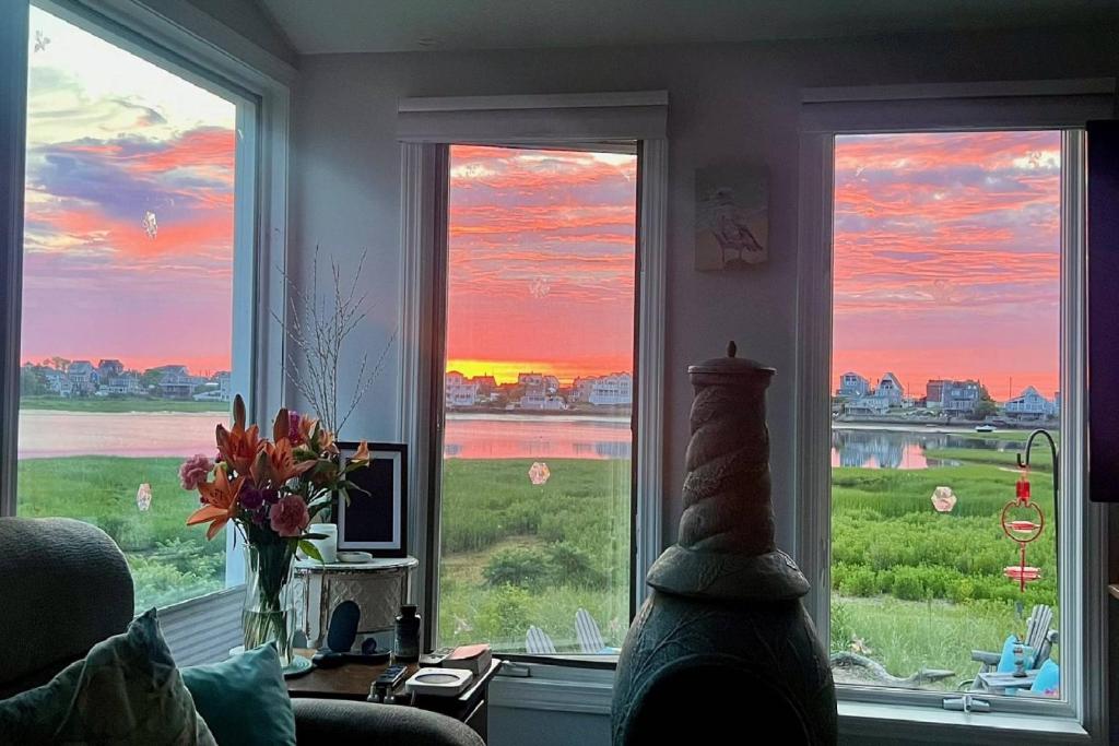 ein Wohnzimmer mit drei Fenstern und Blick auf den Sonnenuntergang in der Unterkunft Island SunRise in Plum Island