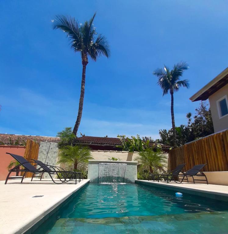 a swimming pool with chairs and palm trees at Pousada Pantai Maresias in Maresias